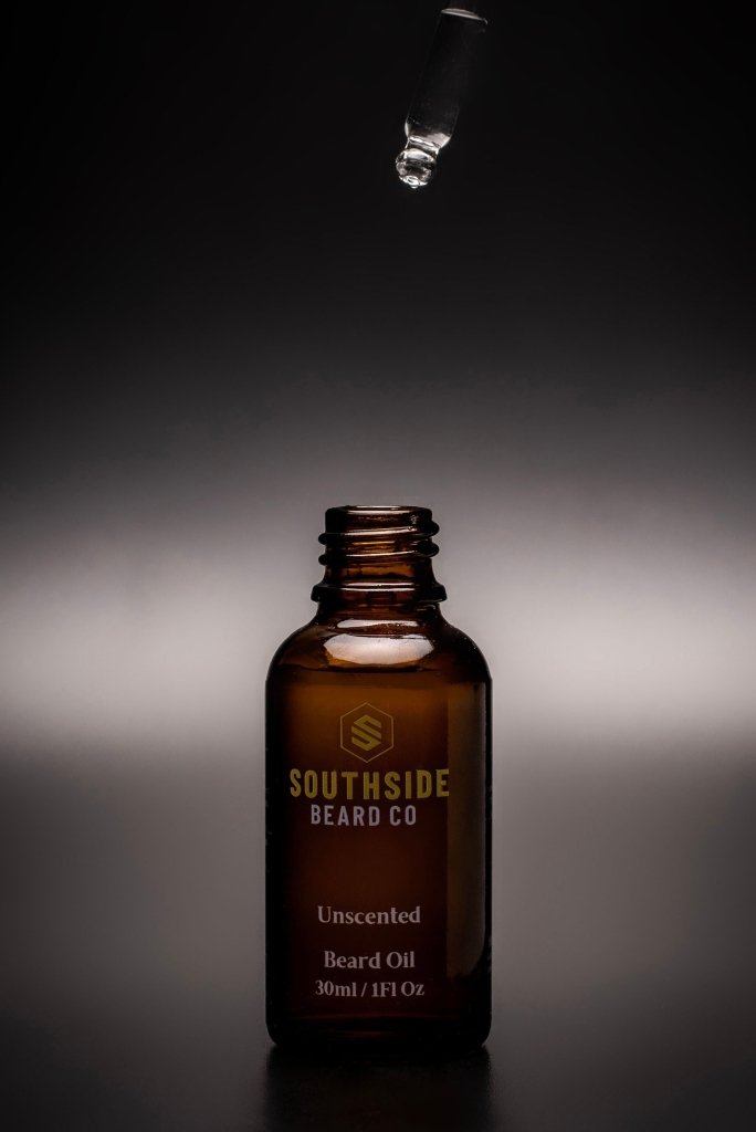 a dark background with a beard oil glass jar and the dropper above it.