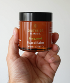 Hand holding a Southside Beard Co. bergamot beard balm jar against a white background