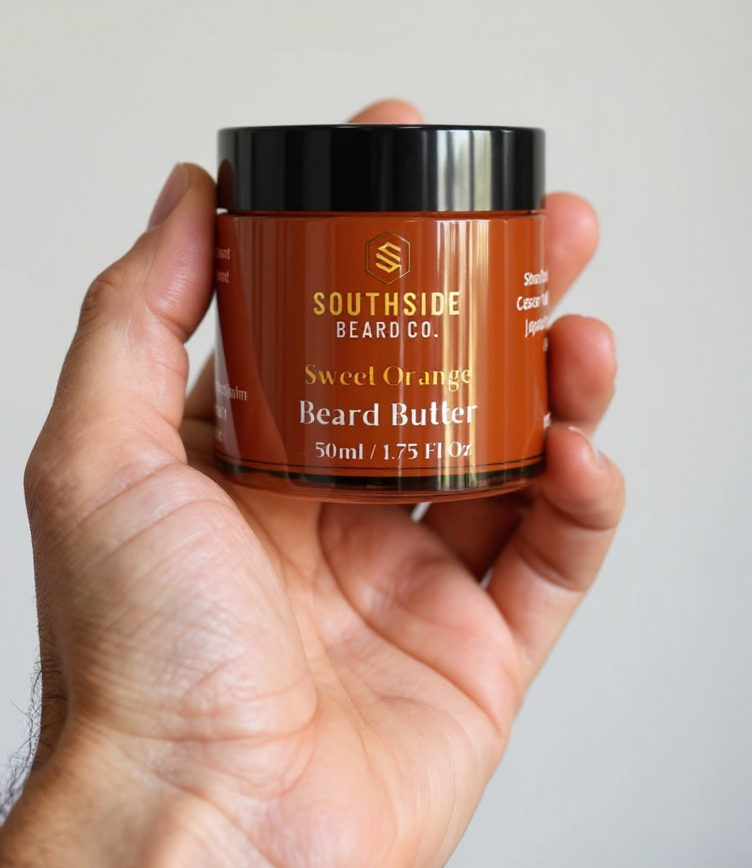 Hand holding a Southside Beard Co sweet orange beard butter jar against a plain background