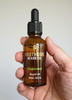 Hand holding a Southside Beard Co.Peppermint beard oil bottle against a plain background