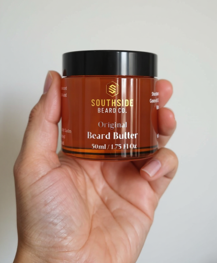 Hand holding a Southside Beard Co unscented beard butter jar against a plain background
