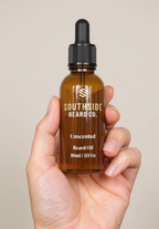 Hand holding a Southside Beard Co. unscented beard oil bottle against a beige background