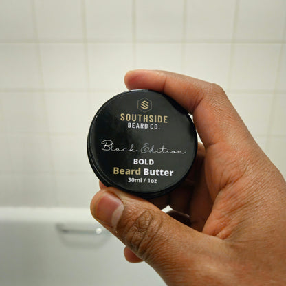 Hand holding a Southside Beard Co. bold beard butter container against a tiled bathroom wall.