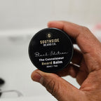 Hand holding a Southside Beard Co. The connoisseur beard balm container against a neutral background