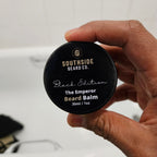 Hand holding a Southside Beard Co. The emperor beard balm container against a neutral background