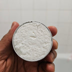 Hand holding a round container with beard butter against a plain background