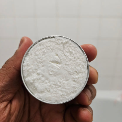 Hand holding a round container with beard butter against a plain background
