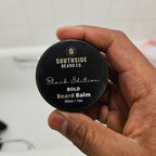 Hand holding a Southside Beard Co.  bold beard balm container with a blurred background