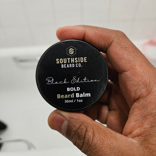Hand holding a Southside Beard Co.  bold beard balm container with a blurred background